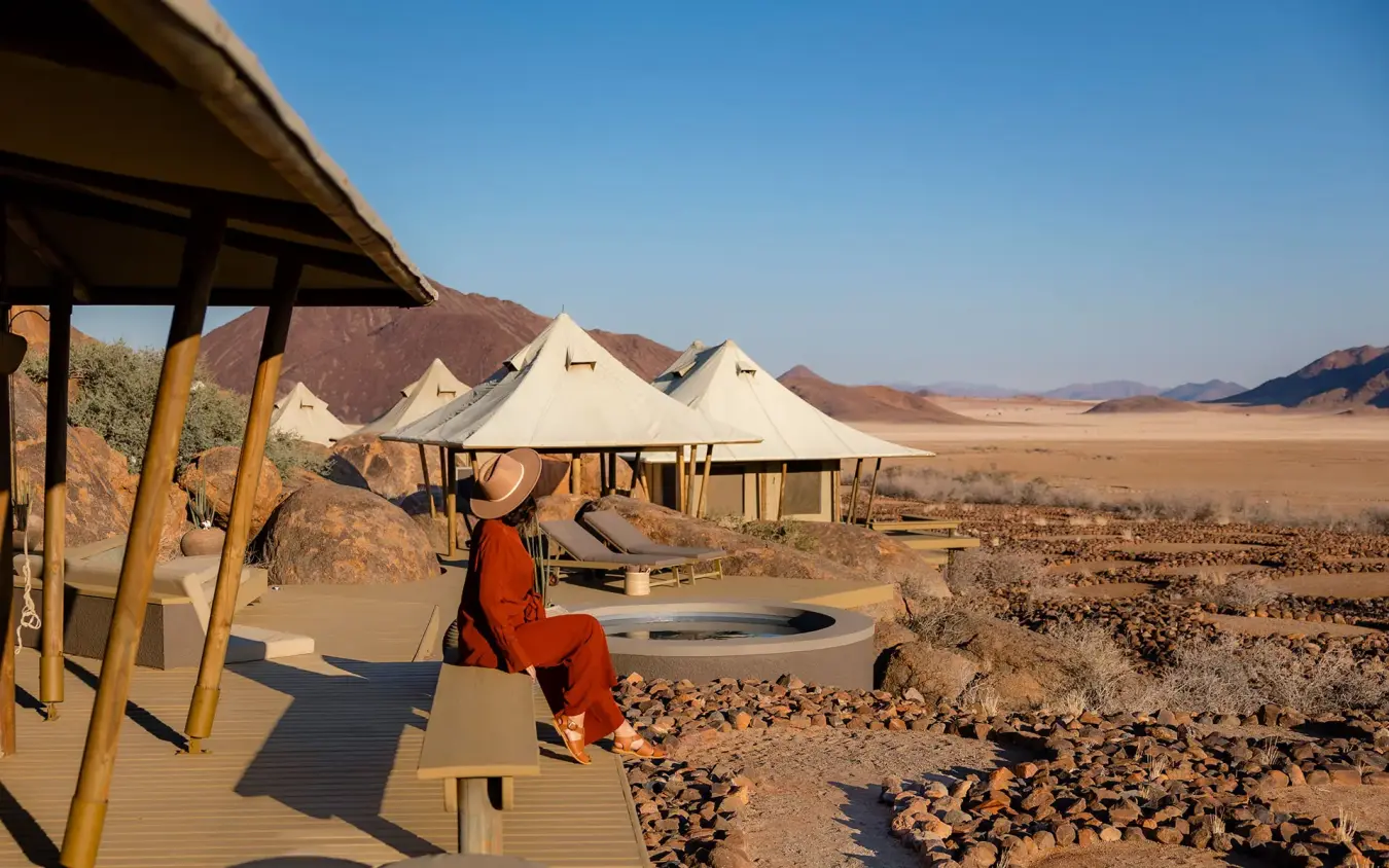 Guest in red sitting on deck overlooking desert landscape, Wolwedans Boulders Camp, NamibRand Private Reserve, Namibia
