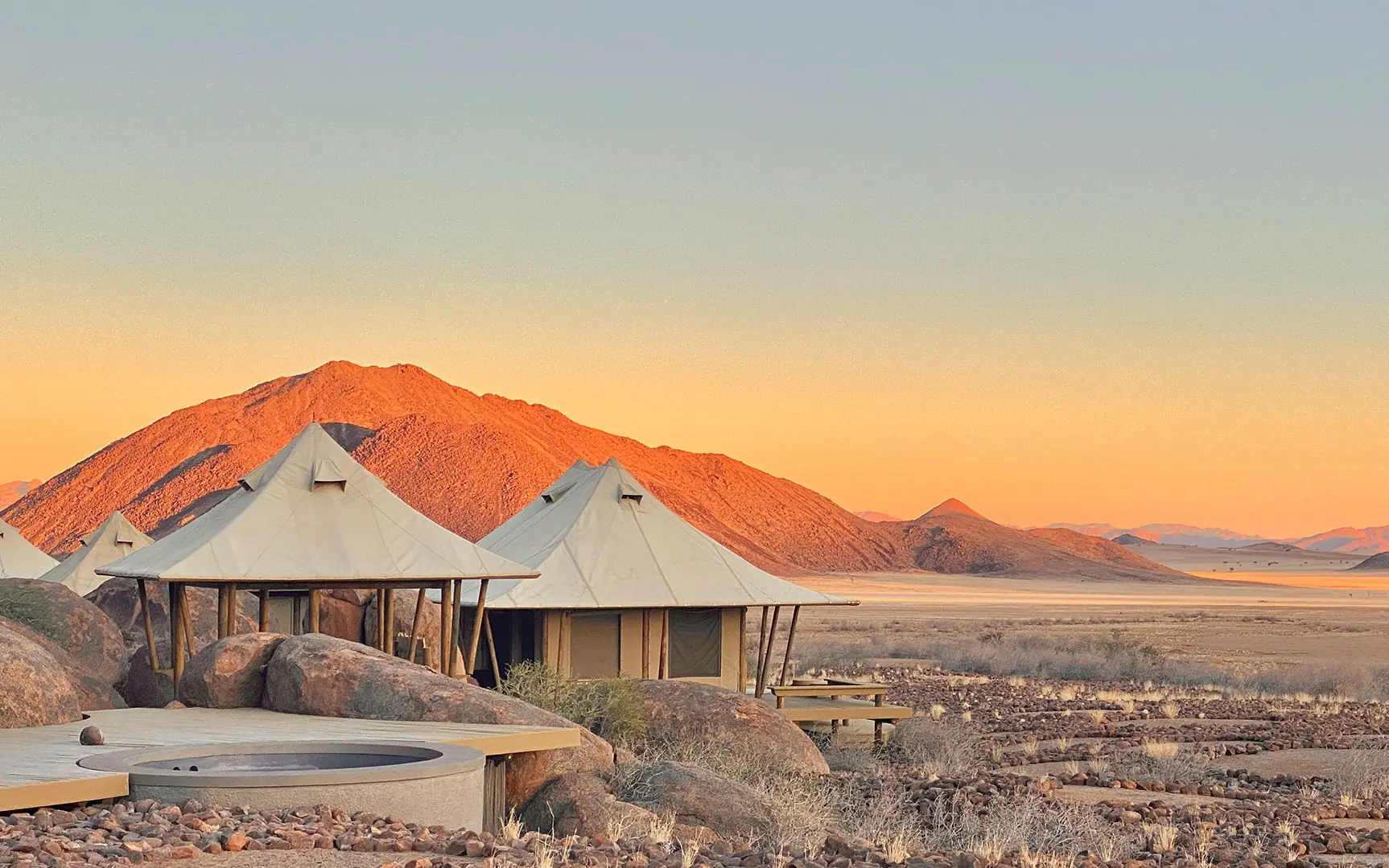 Canvas tent lodge with mountain backdrop at sunset, Wolwedans Boulders Camp, NamibRand Private Reserve, Namibia