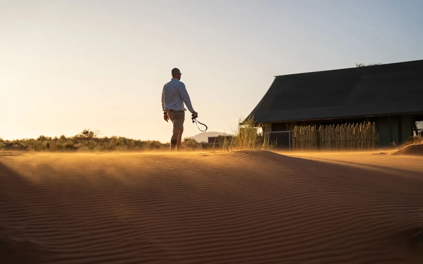 Guest walking across red sand dunes near lodge building, Wolwedans Dune Camp, NamibRand Private Reserve, Namibia