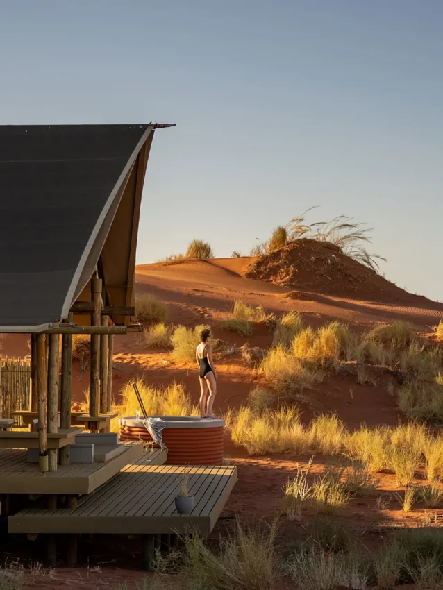 Guest relaxing on wooden deck at sunset with dunes, Wolwedans Dune Camp, NamibRand Private Reserve, Namibia
