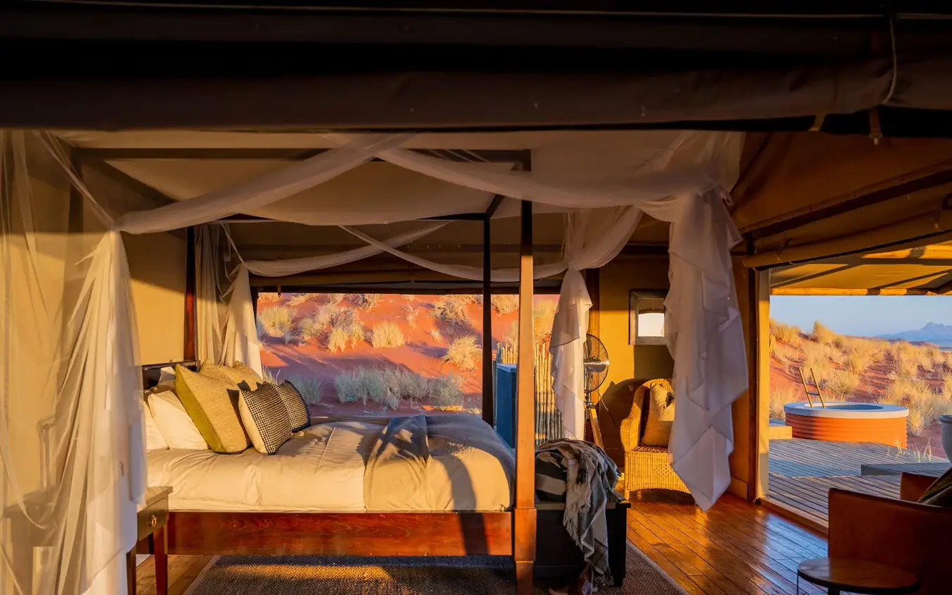 Canopy bed in room overlooking desert landscape at sunset, Wolwedans Dune Camp, NamibRand Private Reserve, Namibia