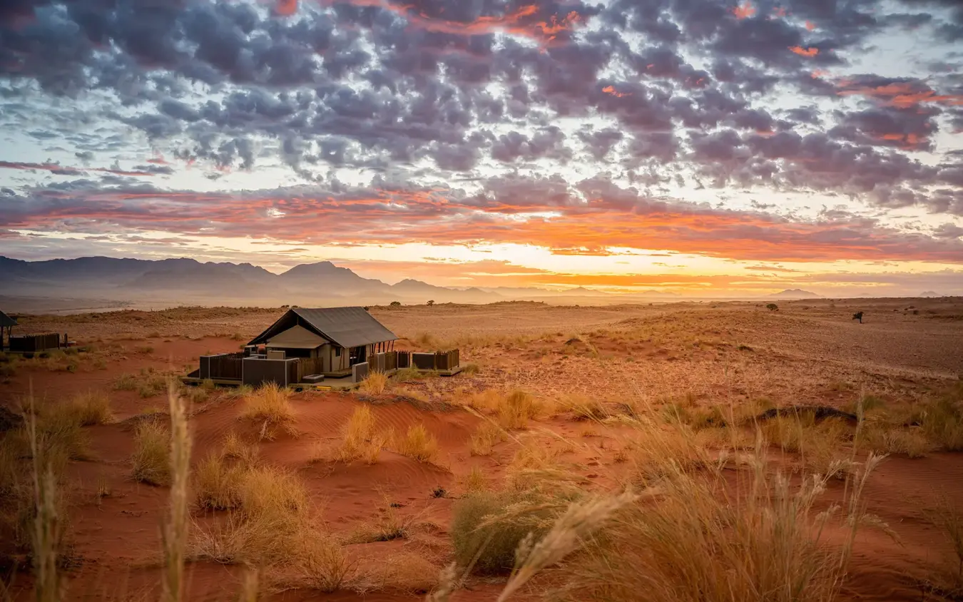 Desert lodge at sunset with golden grassland and mountains, Wolwedans Dune Camp, NamibRand Private Reserve, Namibia