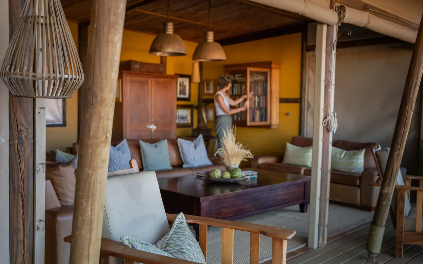 Guest relaxing in open-air lounge with wooden furnishings, Wolwedans Dune Camp, NamibRand Private Reserve, Namibia