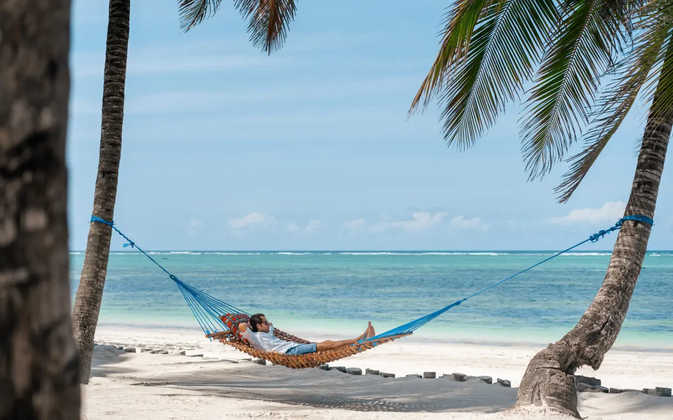 Guest relaxing in hammock between palm trees on beach, Xanadu Villas, Zanzibar & Pemba, Tanzania