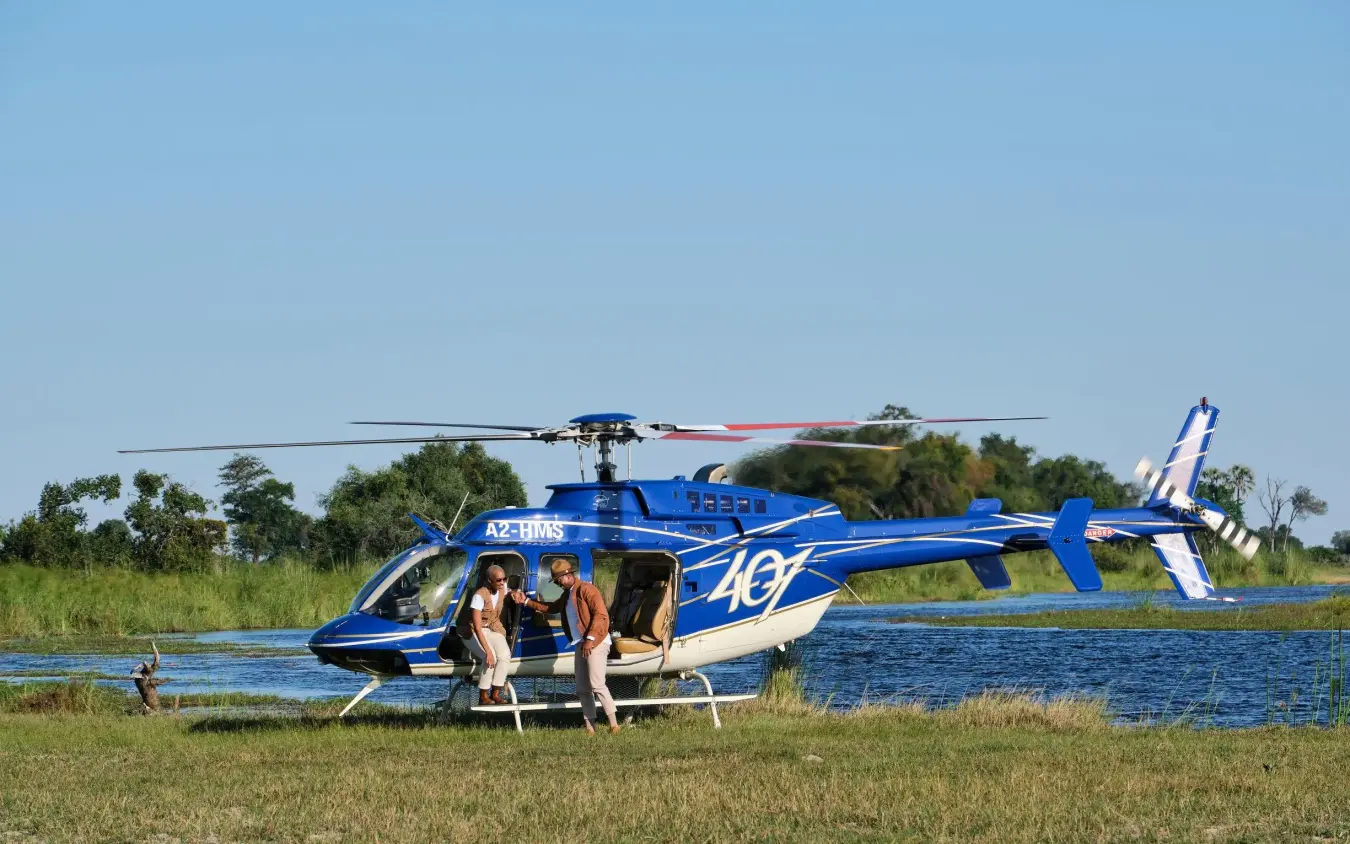 Helicopter with passengers landing near water and grassland, Xigera Lodge, The Okavango Delta, Botswana