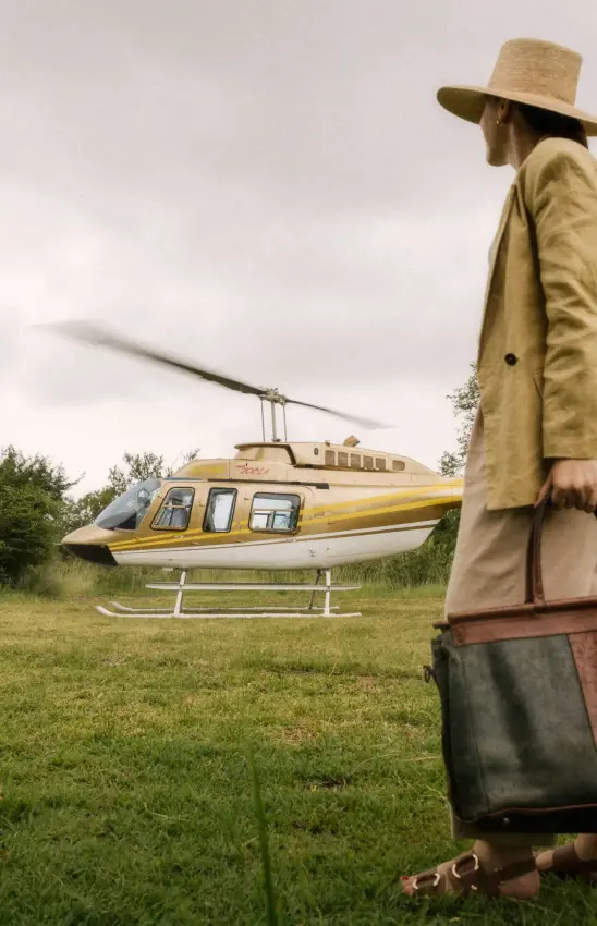 Businessman with briefcase waiting for yellow helicopter on grass airstrip, Zambezi Sands, Victoria Falls, Zimbabwe