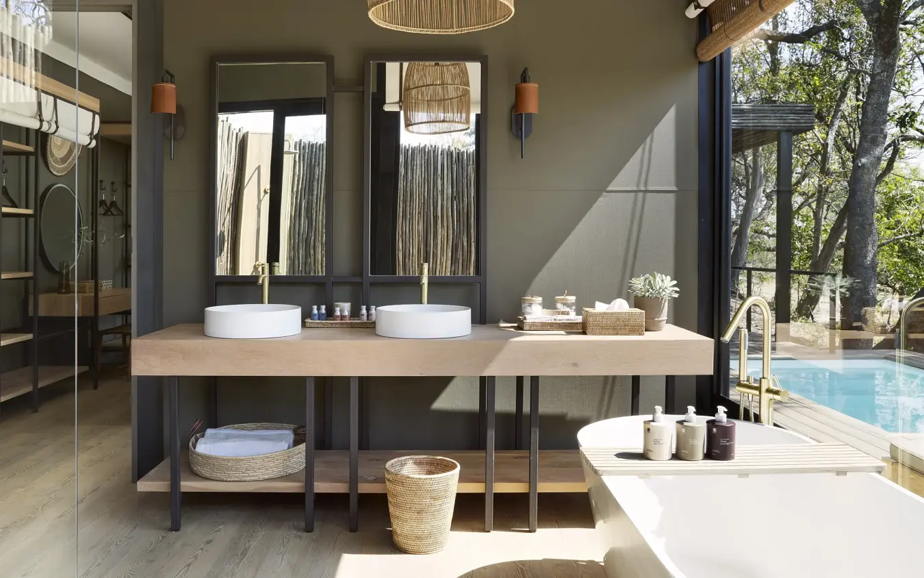 Luxury bathroom with dual vanities and freestanding tub overlooking pool and trees, Zambezi Sands, Victoria Falls, Zimbabwe
