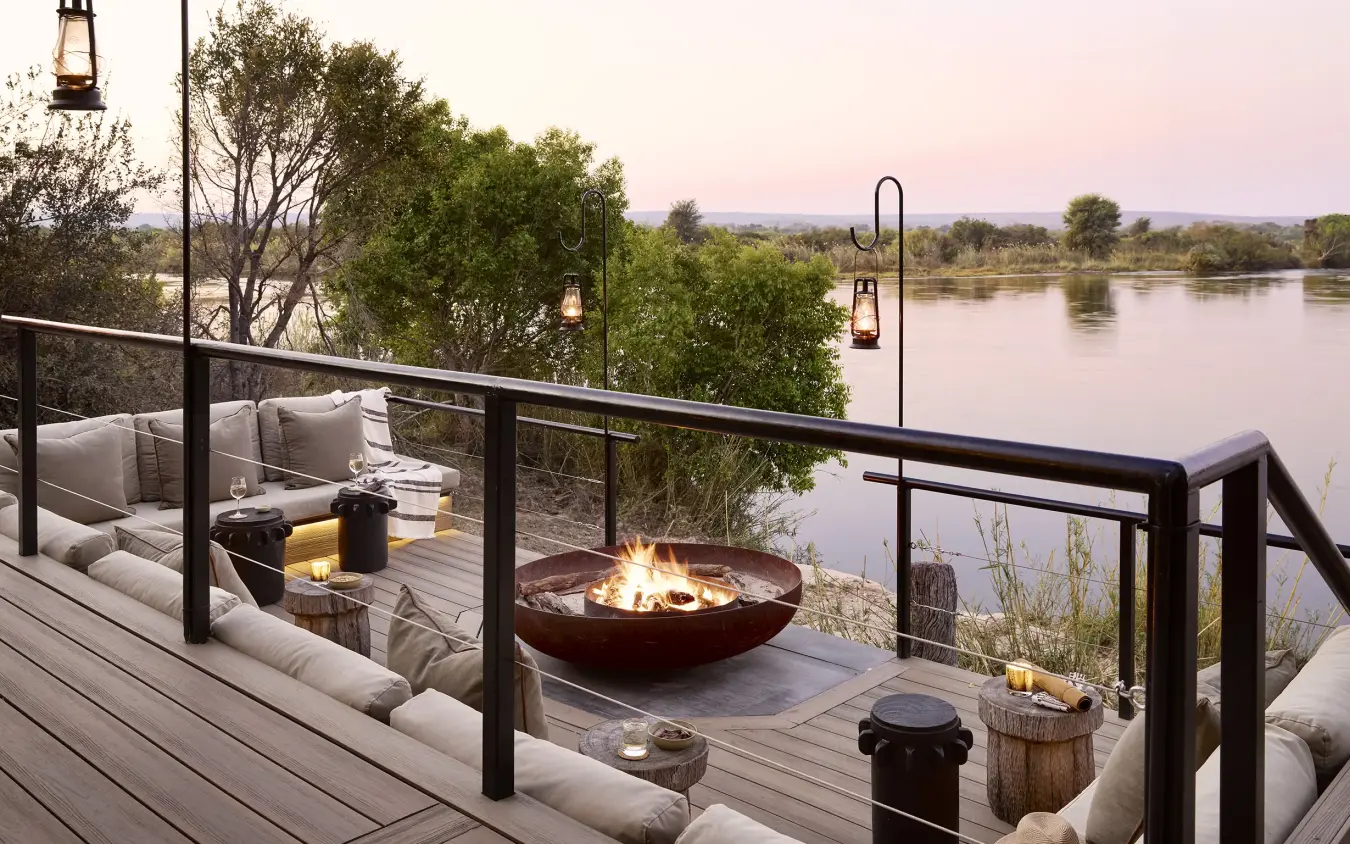 Riverside deck with fire bowl and lounge seating at dusk, Zambezi Sands, Victoria Falls, Zimbabwe