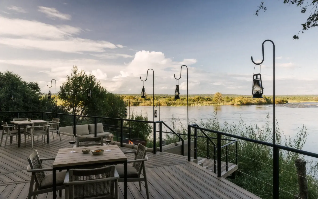 Riverside deck with dining and lounge furniture overlooking river landscape, Zambezi Sands, Victoria Falls, Zimbabwe