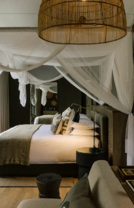 Canopied bed with sheer drapes and woven pendant light in bedroom, Zambezi Sands, Victoria Falls, Zimbabwe