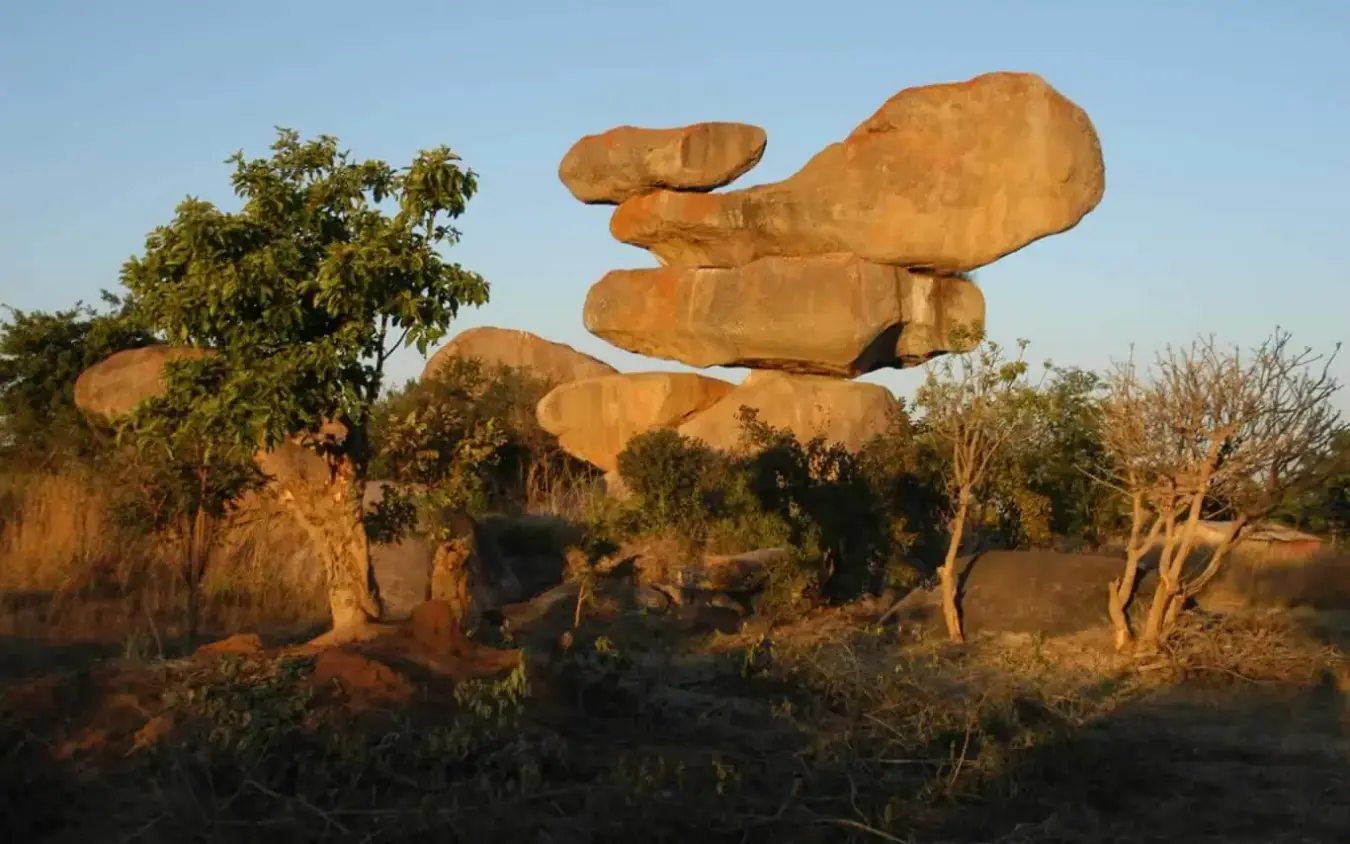 Stacked granite boulders in savanna landscape with scattered trees at sunset, Zambezi Sands, Victoria Falls, Zimbabwe