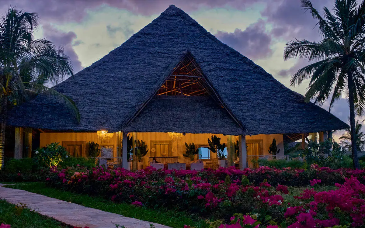 Thatched-roof lodge building illuminated at dusk with flowering gardens, Zawadi Hotel, Zanzibar & Pemba, Tanzania