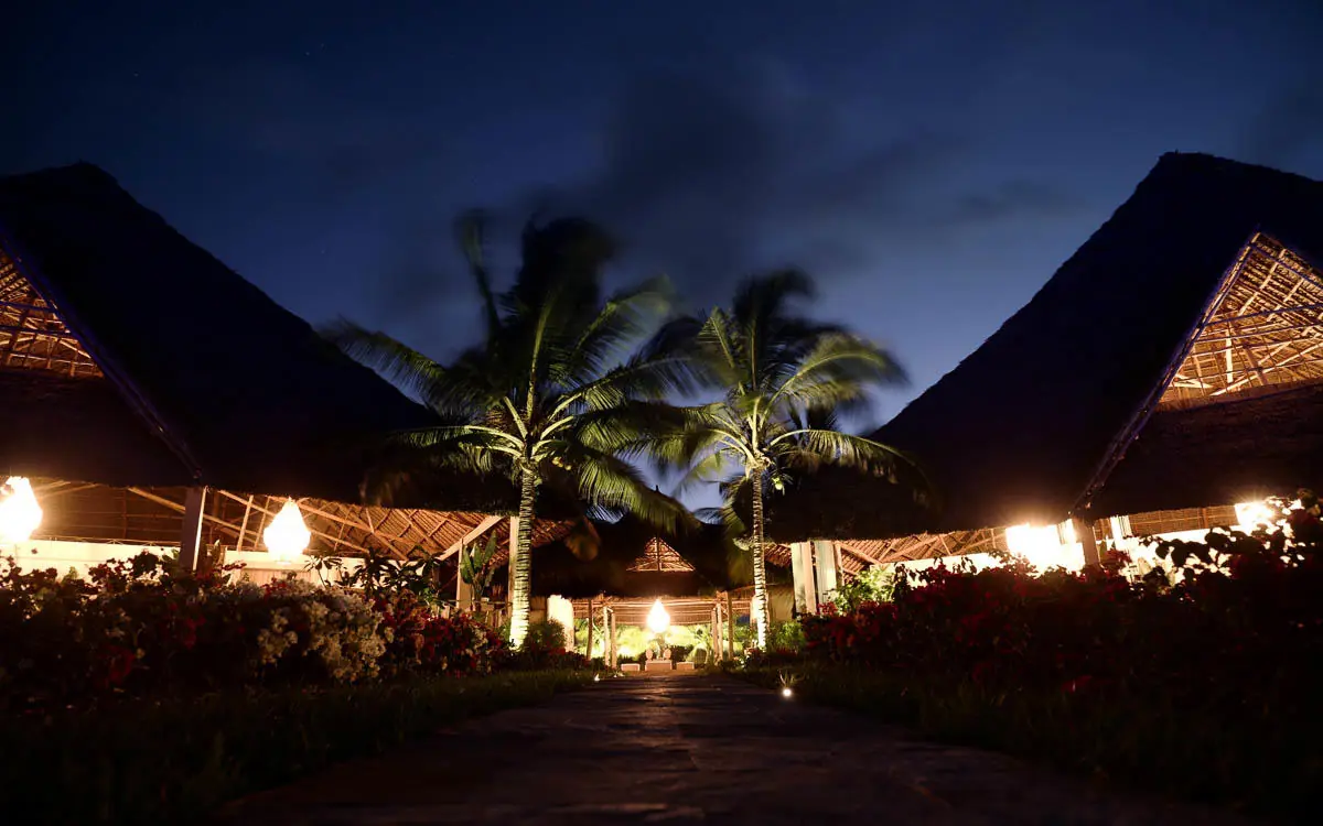 Illuminated thatch-roof structures with palm trees at dusk, Zawadi Hotel, Zanzibar & Pemba, Tanzania