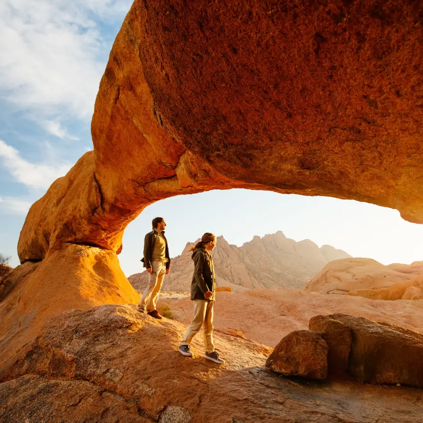 Hikers explore natural rock arch at sunset in desert