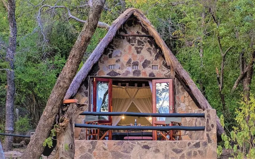Stone lodge with thatched roof nestled among forest trees, Big Cave Camp, Matobo, Zimbabwe