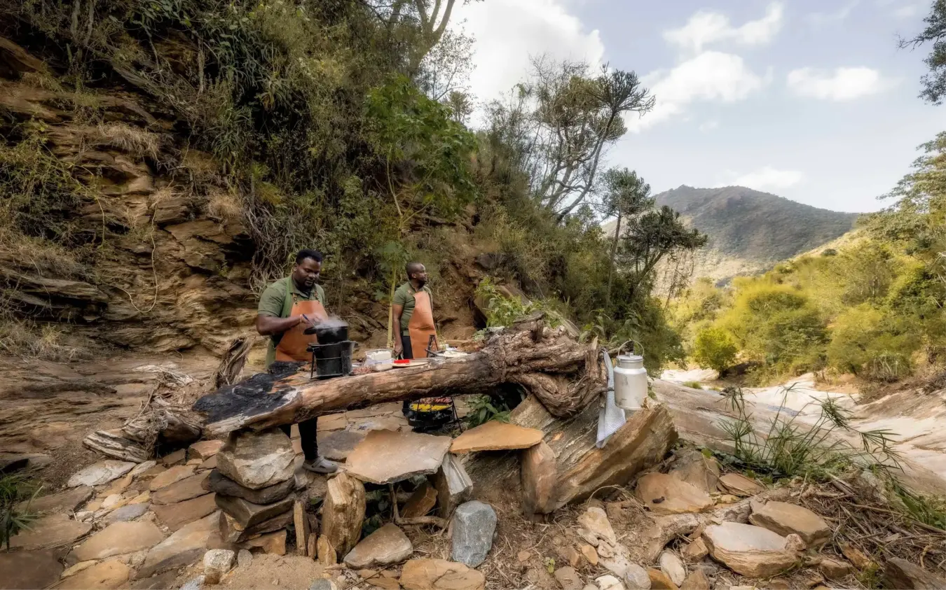 Hikers preparing camp at riverside rest stop in mountain valley, Desert Rose, Northern Kenya, Kenya