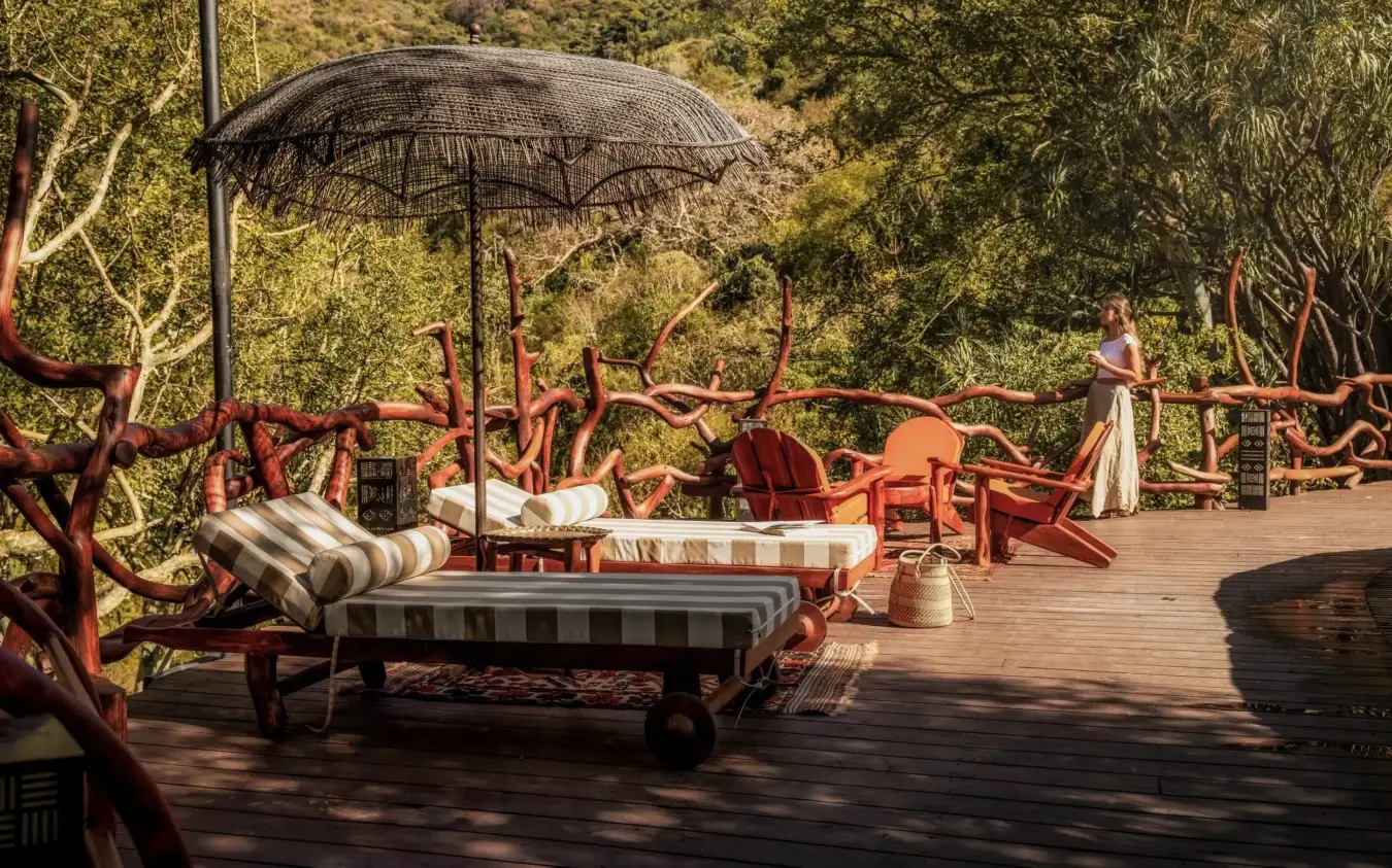 Wooden deck lounge area with red sculptural branches and striped daybeds under shade umbrella, Desert Rose, Northern Kenya, Kenya