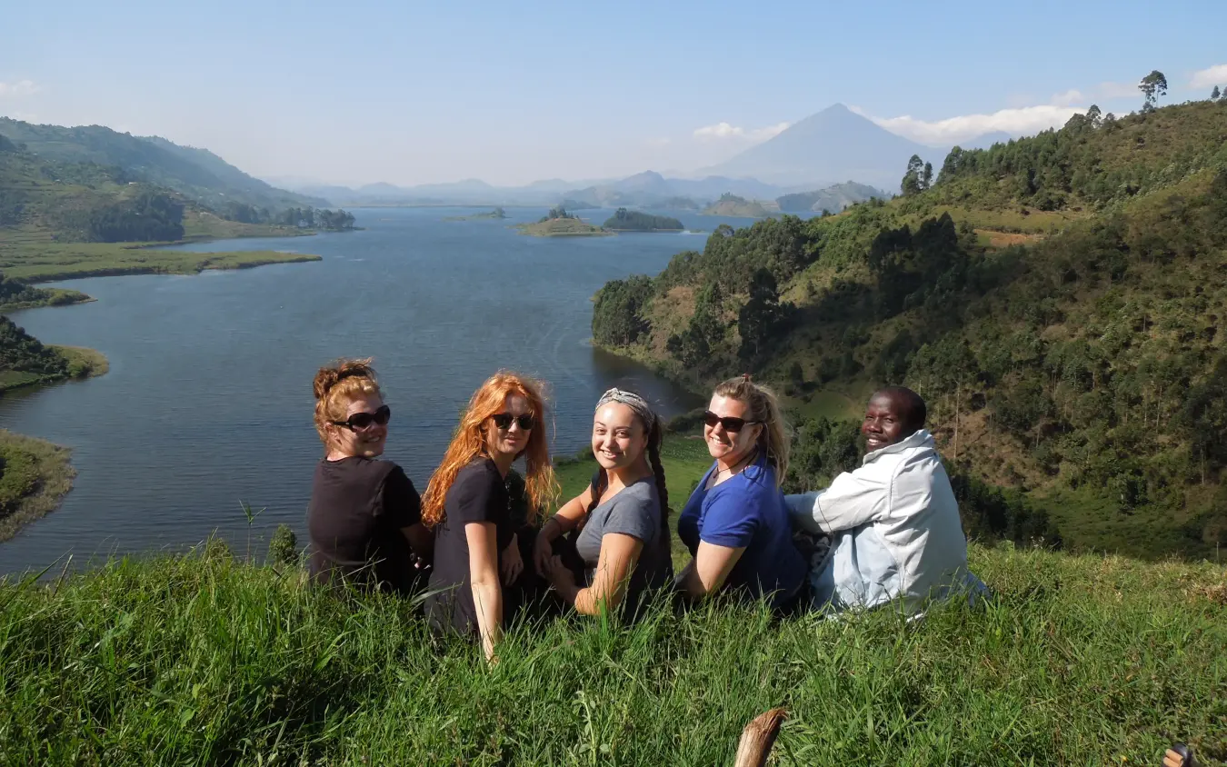 Group of travelers seated on hillside overlooking scenic lake and mountain landscape