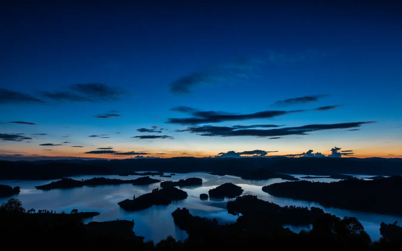 Silhouetted forested islands dotting lake at twilight with blue sky
