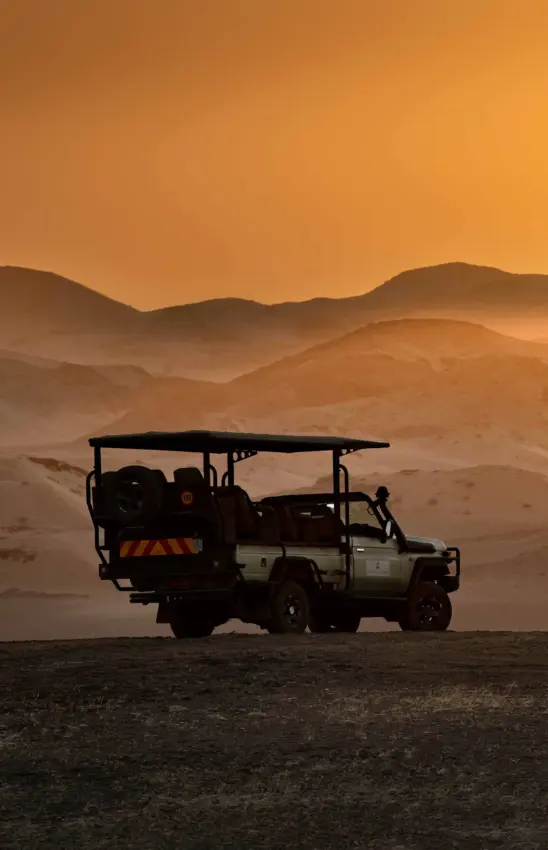 Safari vehicle silhouetted against desert dunes at sunset, Hoanib Elephant Camp, Skeleton Coast, Namibia