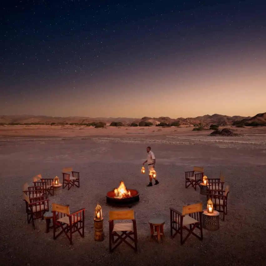Campfire setup with chairs and lanterns in desert landscape at dusk, Hoanib Elephant Camp, Skeleton Coast, Namibia