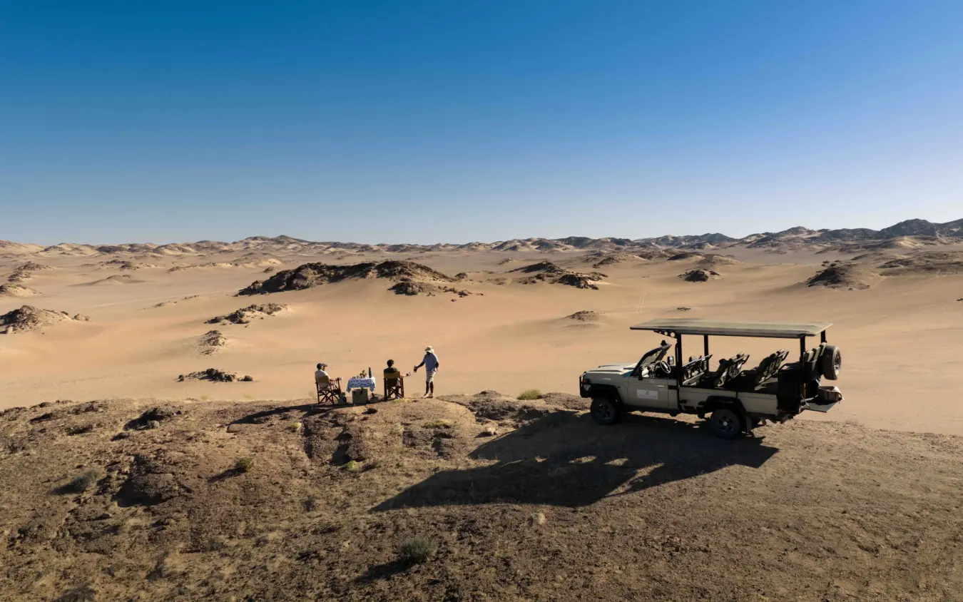 Safari vehicle with guests on rocky outcrop in desert landscape, Hoanib Elephant Camp, Skeleton Coast, Namibia