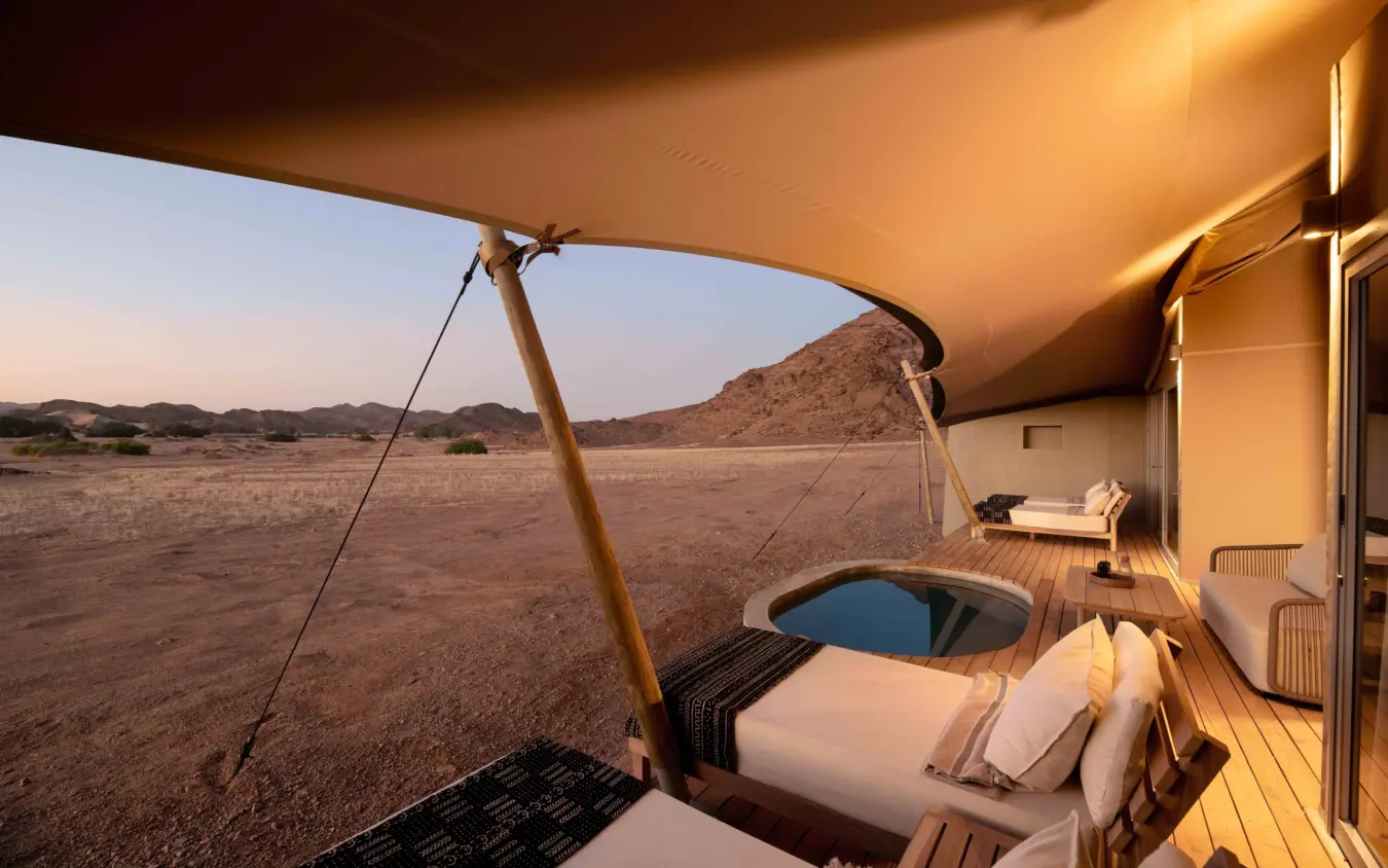 Open-air bedroom tent with bed overlooking arid savanna landscape at dusk, Hoanib Elephant Camp, Skeleton Coast, Namibia