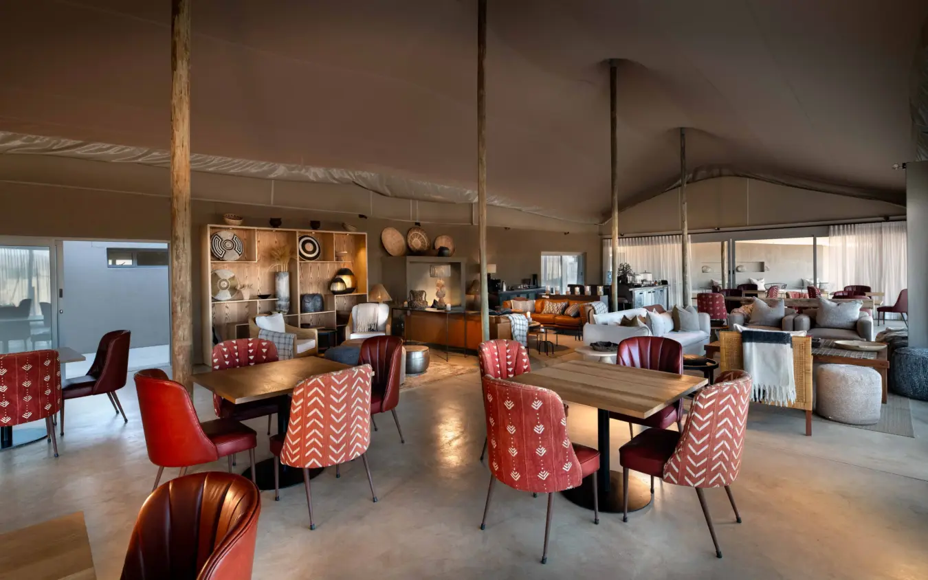 Open-plan dining and lounge area with red patterned chairs and wooden tables, Hoanib Elephant Camp, Skeleton Coast, Namibia