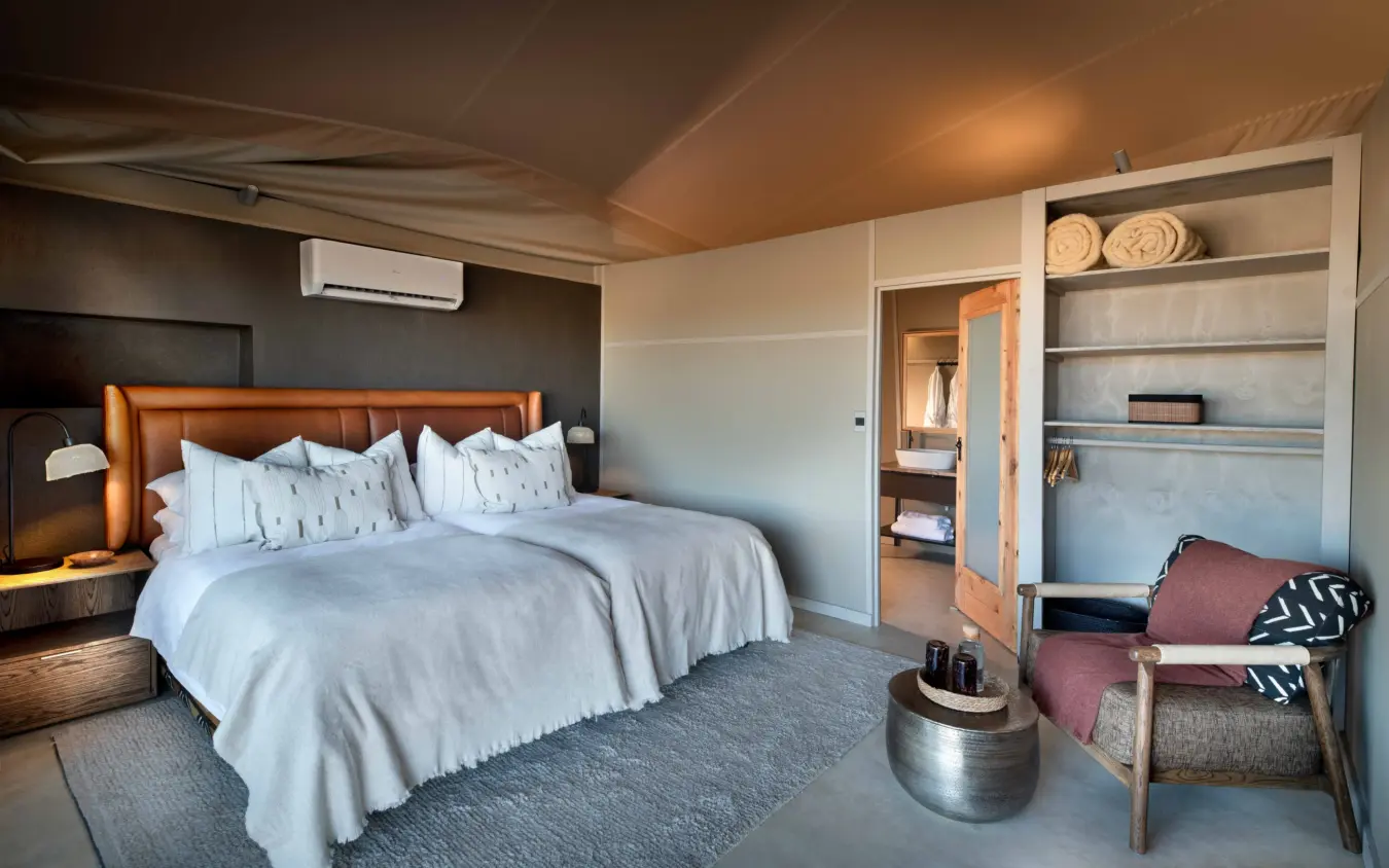Modern safari lodge bedroom with leather bed frame and views to ensuite, Hoanib Elephant Camp, Skeleton Coast, Namibia