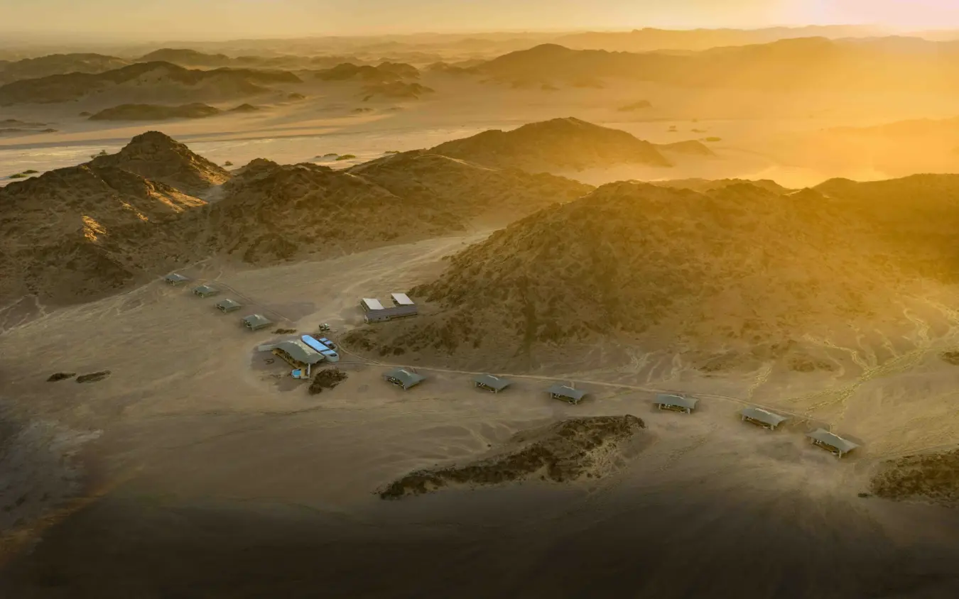 Luxury camp with safari vehicles parked in desert valley at sunset, Hoanib Elephant Camp, Skeleton Coast, Namibia