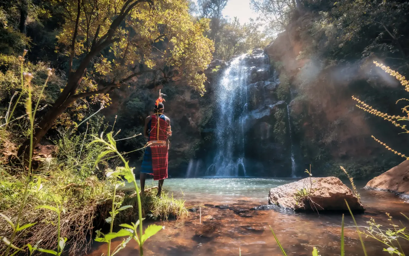 Maasai warrior standing at waterfall pool in forested canyon, Kifaru House, Laikipia Highlands, Kenya