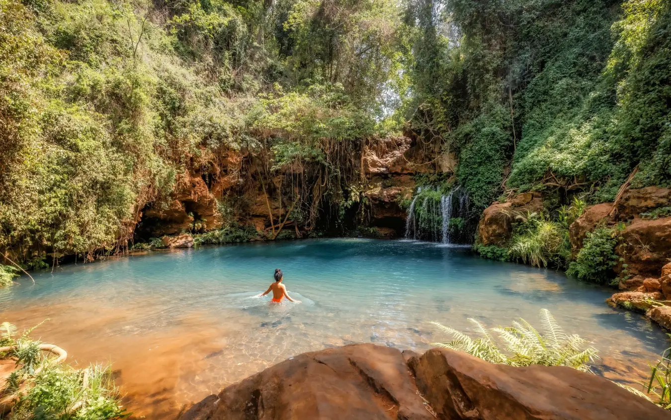 Tourist swimming in natural pool beneath waterfall and cave opening, Kifaru House, Laikipia Highlands, Kenya