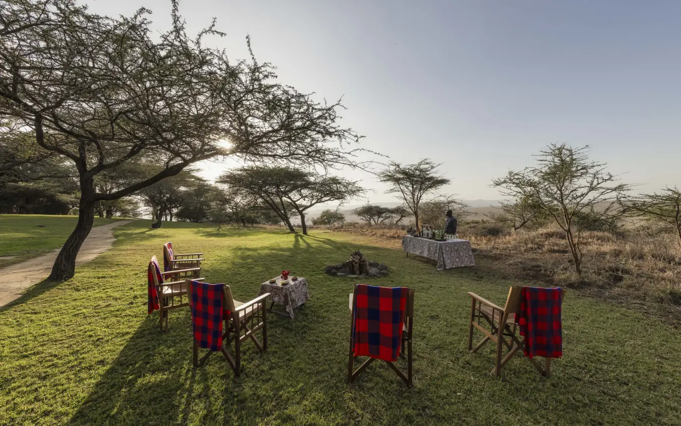 Outdoor dining setup with red blankets on chairs in savanna grassland, Kifaru House, Laikipia Highlands, Kenya