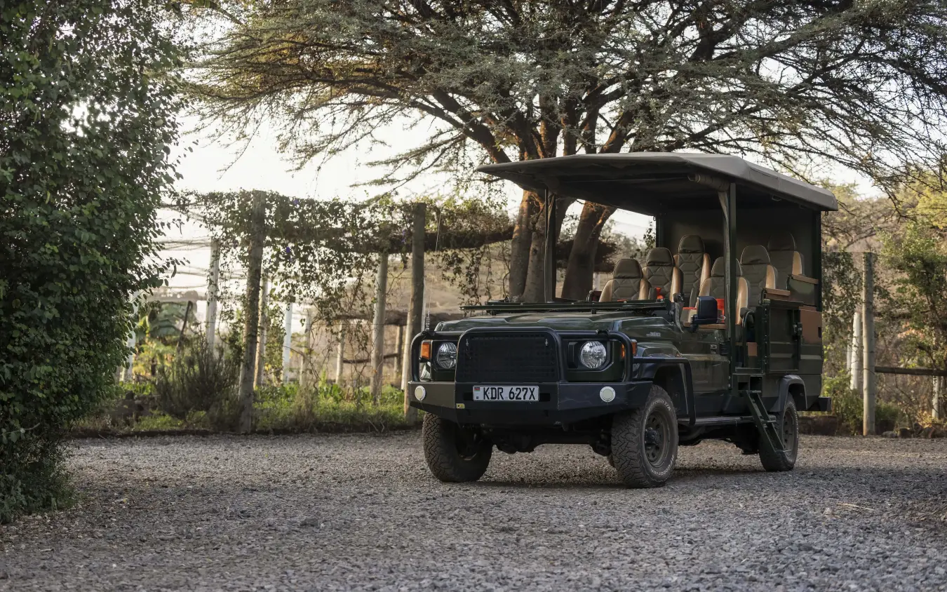 Classic safari vehicle parked beneath mature acacia tree near stone structures, Kifaru House, Laikipia Highlands, Kenya