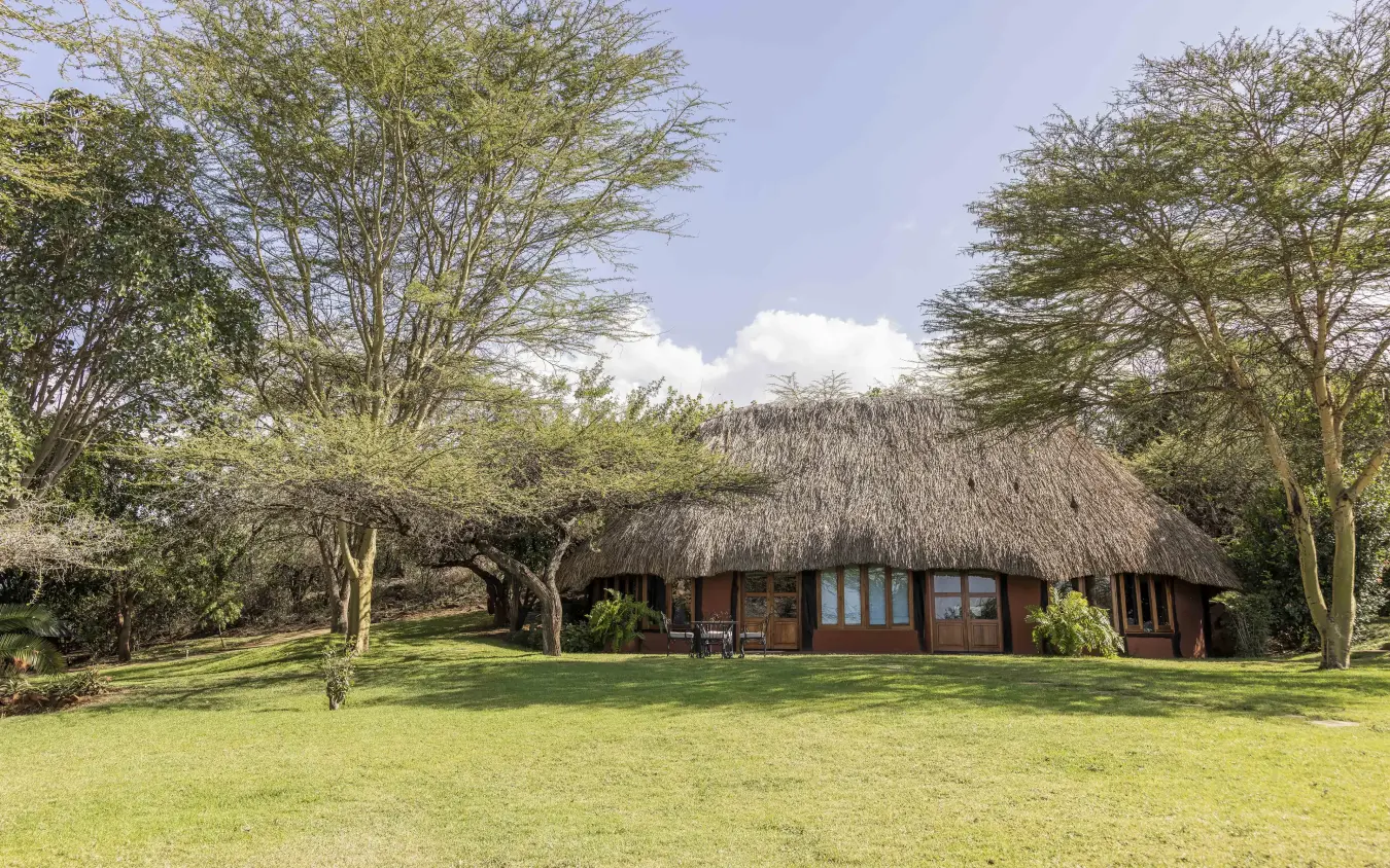 Thatched roof lodge with wooden deck among acacia trees and manicured lawn, Kifaru House, Laikipia Highlands, Kenya