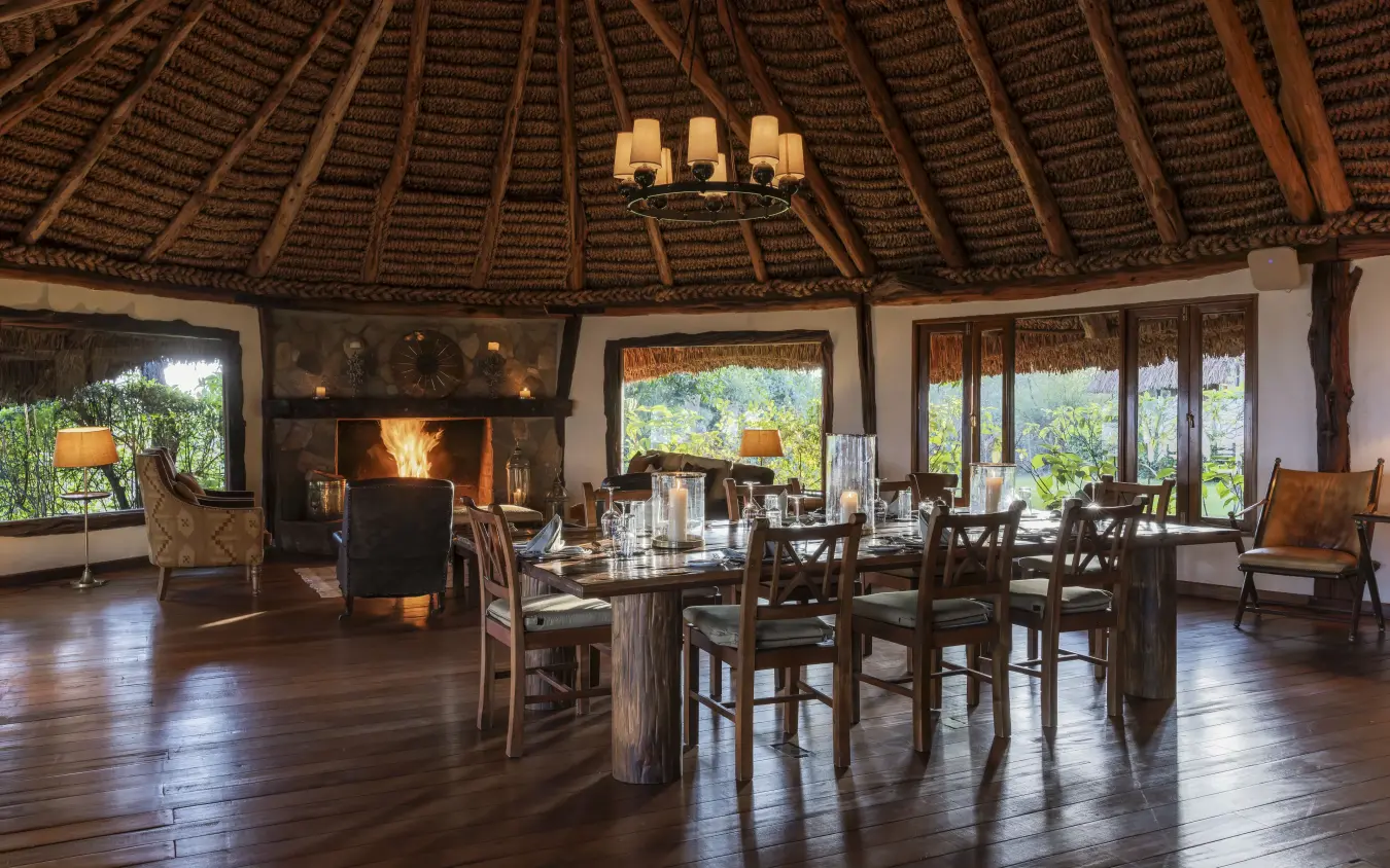 Circular lodge interior with fireplace, dining table and thatch roof, Kifaru House, Laikipia Highlands, Kenya