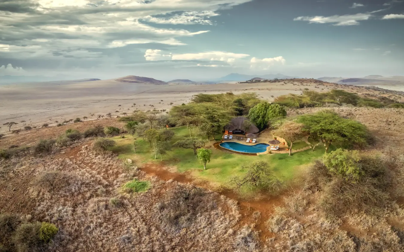 Luxury lodge with blue pool nestled among acacia trees in arid savanna landscape, Kifaru House, Laikipia Highlands, Kenya