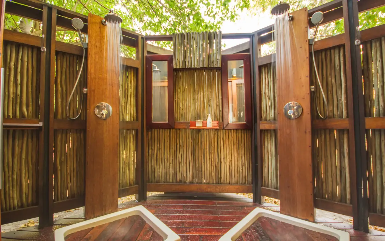 Outdoor shower pavilion with wooden doors and flowing curtains under trees, Kwando Lebala Camp, Linyanti Wildlife Reserve, Botswana
