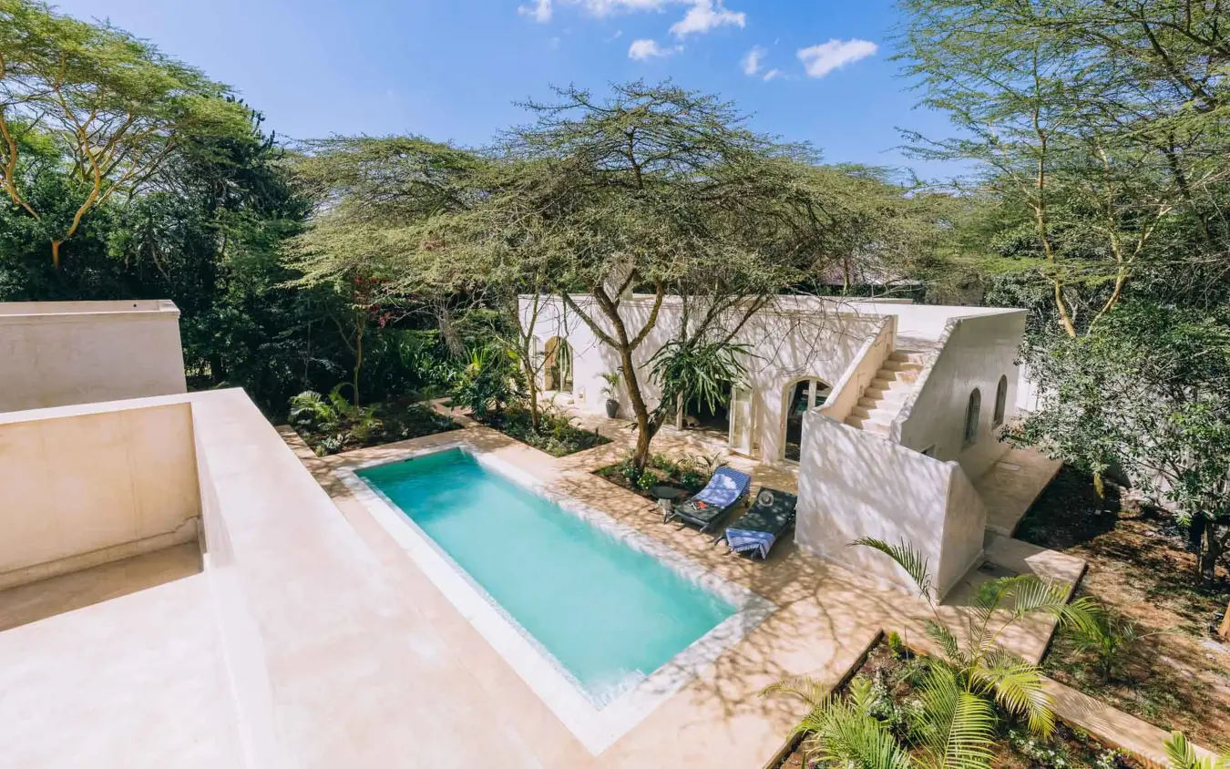 Rectangular swimming pool surrounded by white architecture and shade trees, Manzili House, Nairobi, Kenya