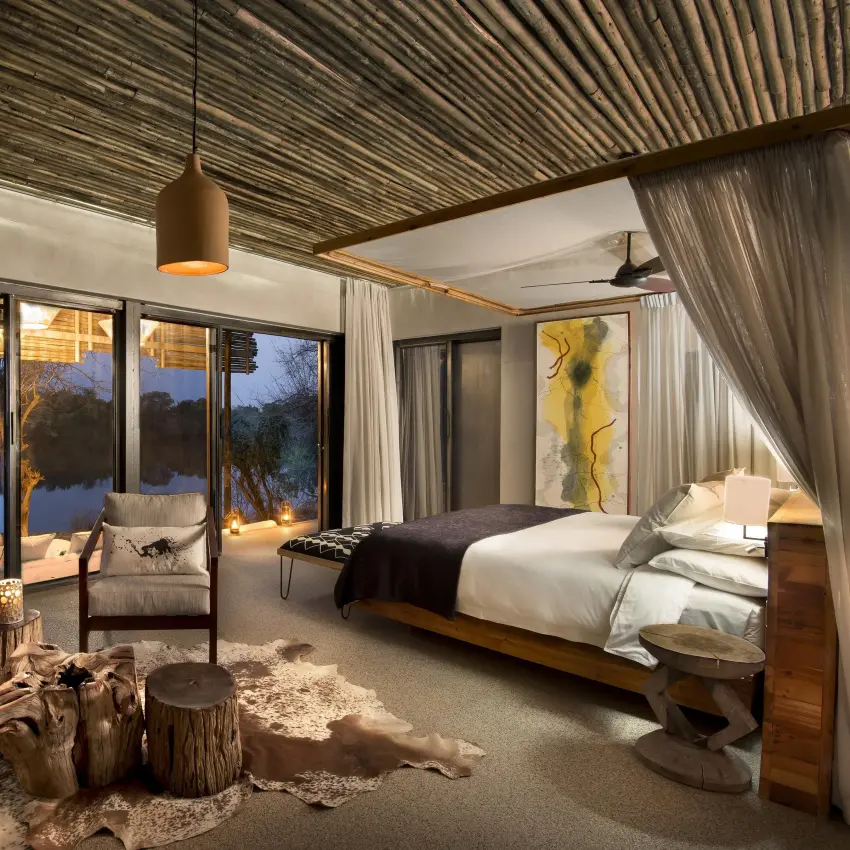 Luxury bedroom with floor-to-ceiling windows overlooking water, Matetsi River Lodge, Victoria Falls, Zimbabwe