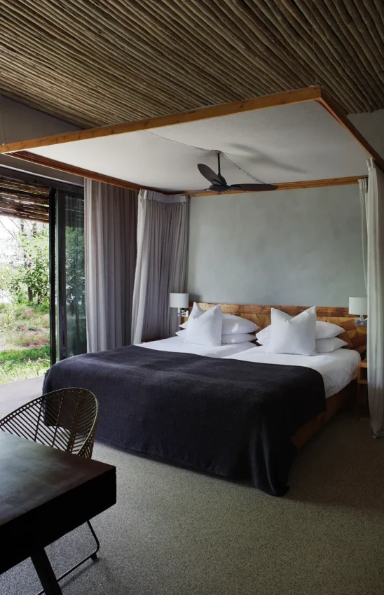 Luxury canopy bed with wooden frame in modern safari bedroom with garden view, Matetsi River Lodge, Victoria Falls, Zimbabwe