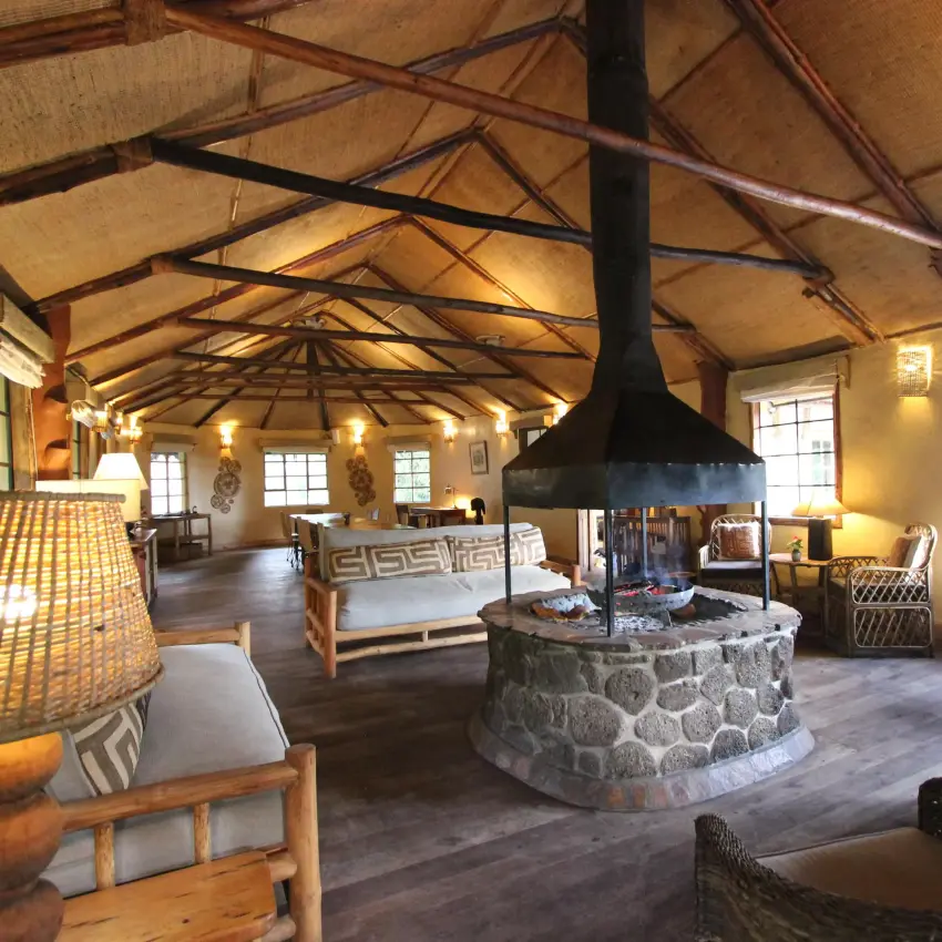 Open-plan lounge with central fireplace and wooden beams, Mount Gahinga Lodge, Mgahinga National Park, Uganda