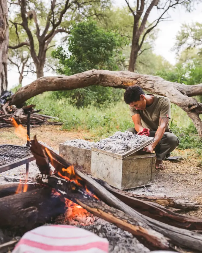 Person tending to cooking fire in bush camp setting