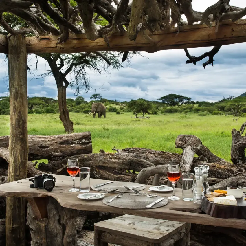 Outdoor dining table set with savanna wildlife visible beyond, Ol Donyo Lodge, Amboseli and Chyulu Hills, Kenya