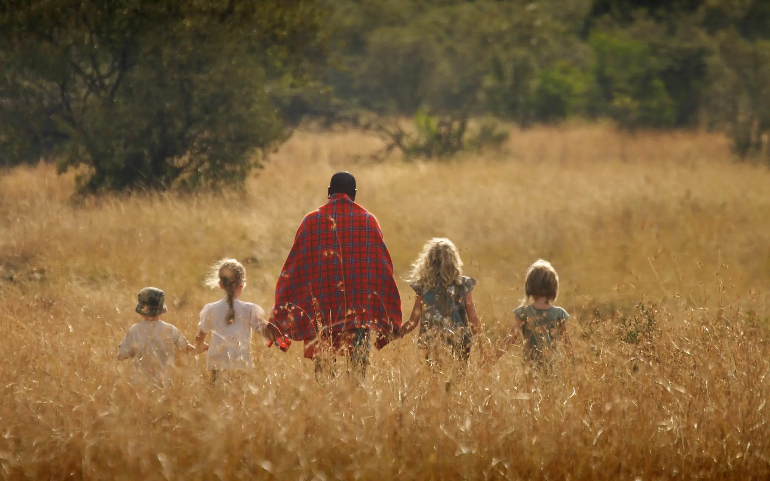 Adult and children walking through golden grassland together