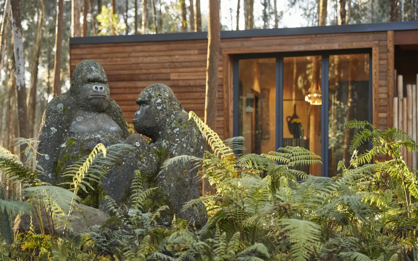 Stone gorilla sculptures in lush fern garden beside wooden lodge, Gorilla’s Nest, Volcanoes National Park, Rwanda