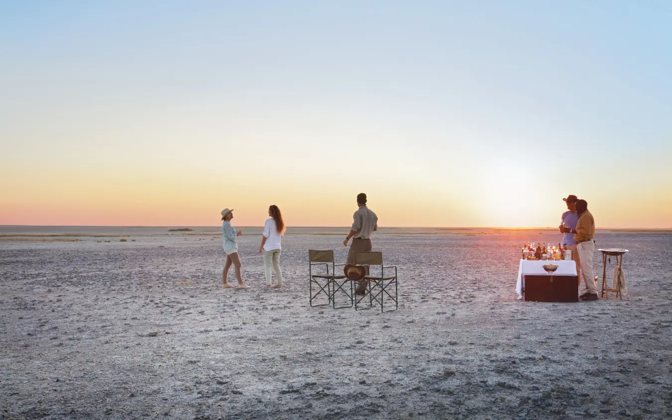 Group enjoying sunset drinks on vast salt pan landscape, San Camp, Makgadikgadi Pans, Botswana