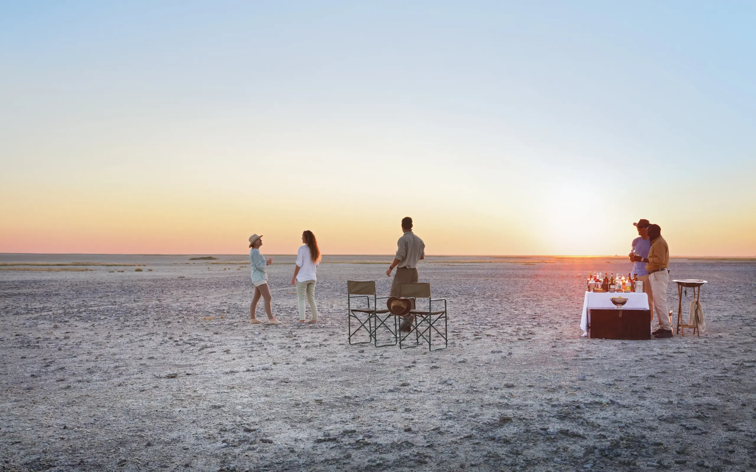 Group enjoying sunset drinks on vast salt pan landscape, San Camp, Makgadikgadi Pans, Botswana