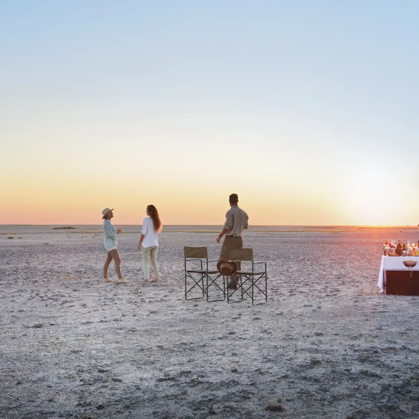 Group enjoying sunset drinks on vast salt pan landscape, San Camp, Makgadikgadi Pans, Botswana