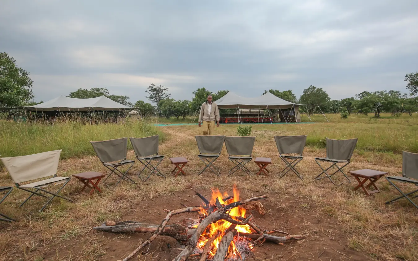 Campfire with canvas chairs and safari tents in savanna grassland, Serengeti North Wilderness Camp, Serengeti National Park, Tanzania